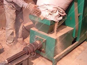 a worker is put sawdust into the screw briquette machine